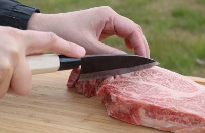 写真：屋外で分厚い牛肉を切ろうとしている様子